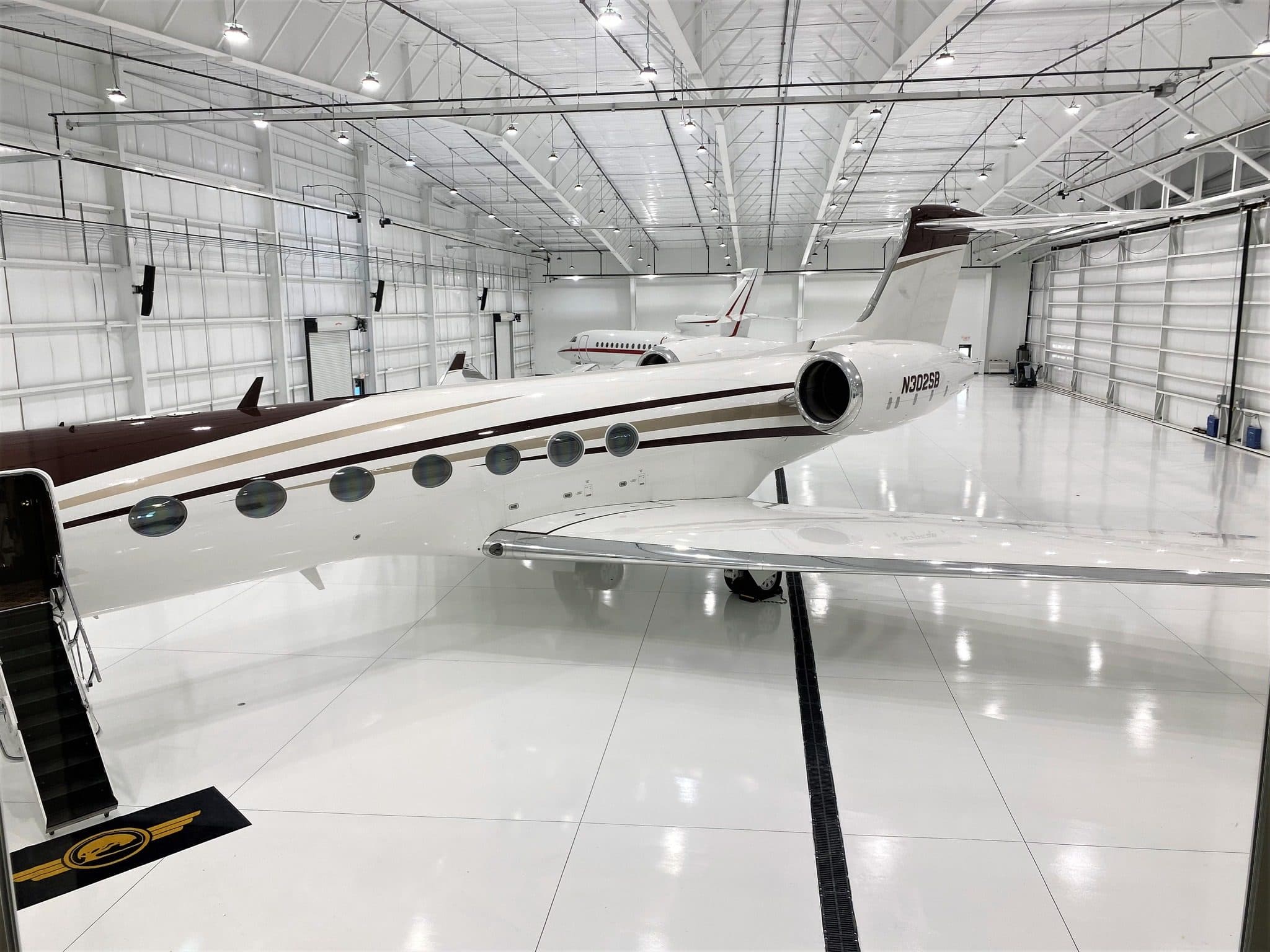 A private jet parked on the white floor of Schell Hangar under rows of lights