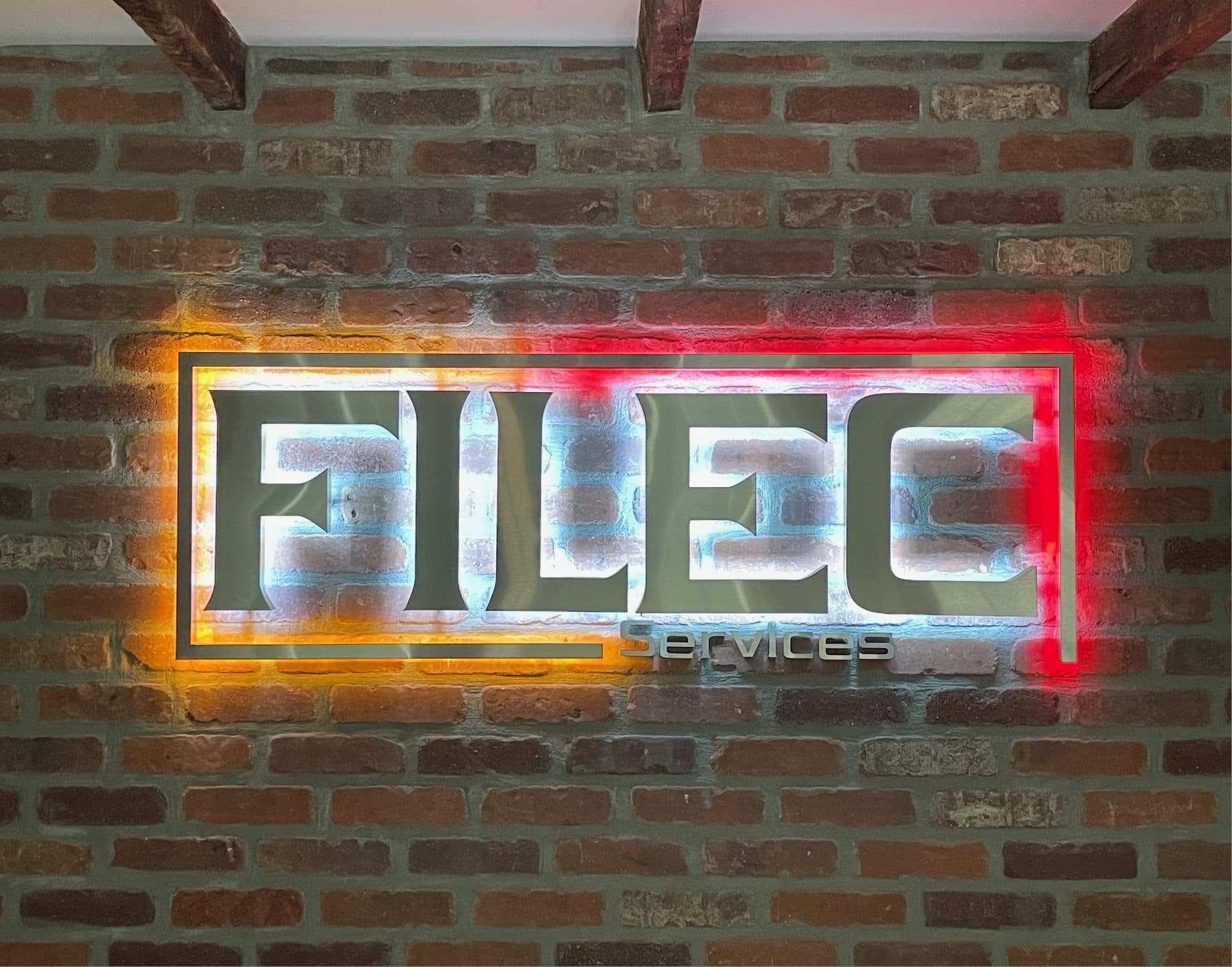 The Filec sign backlit in orange and red on a brick wall