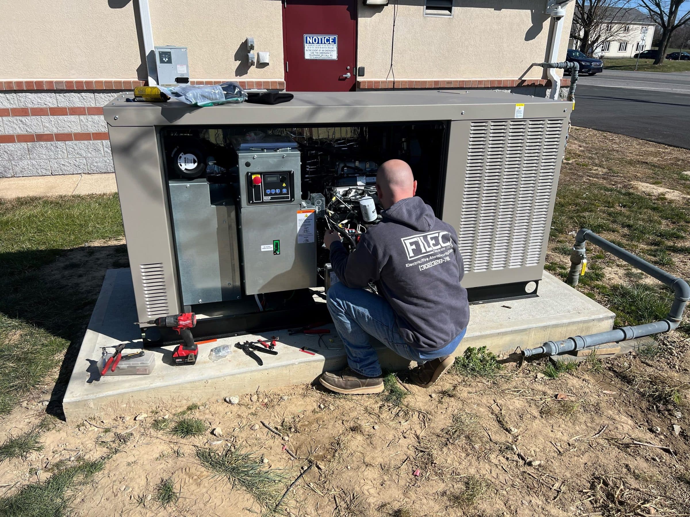 A Filec electrician kneeling to wire a standby generator