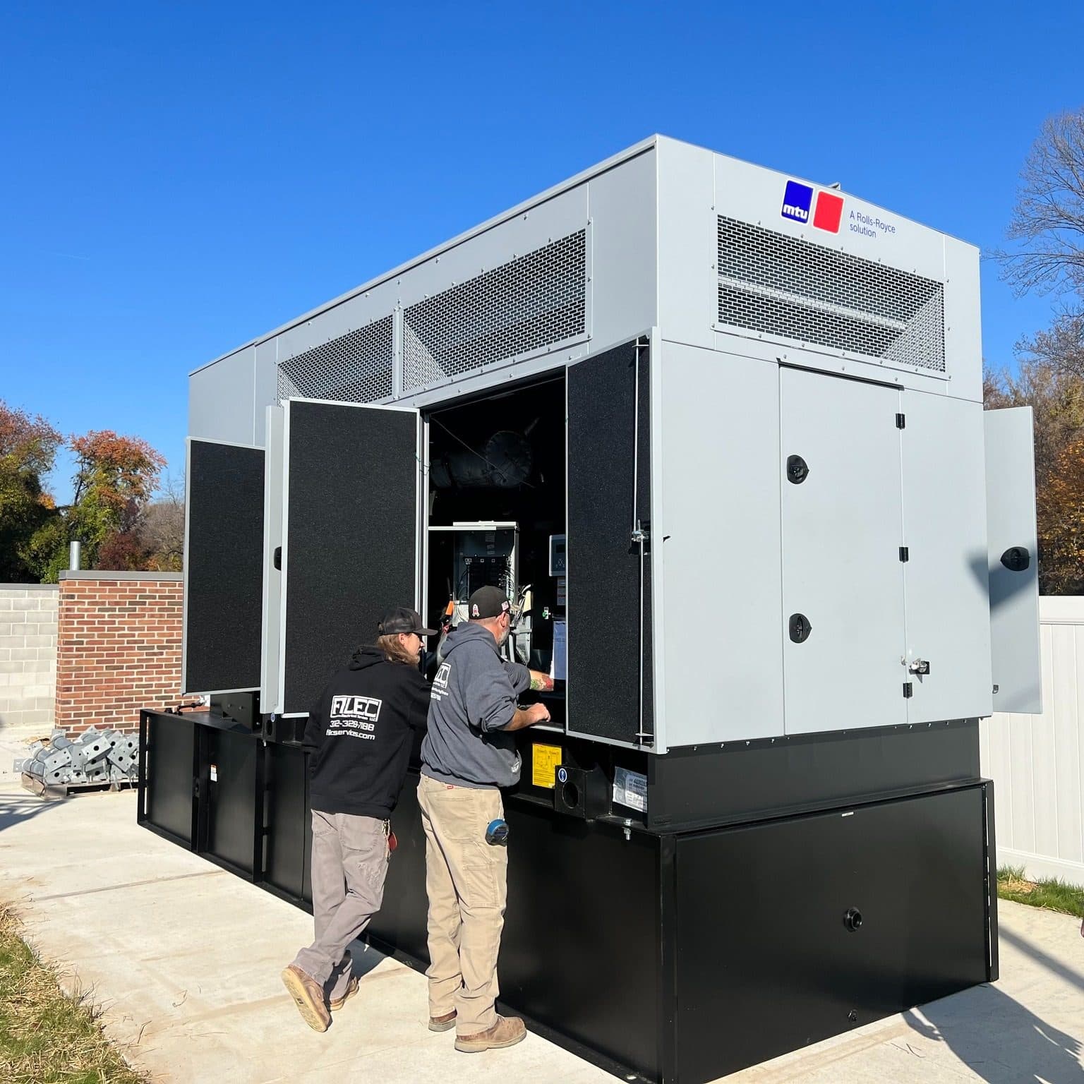 Two Filec electricians working inside a large generator enclosure
