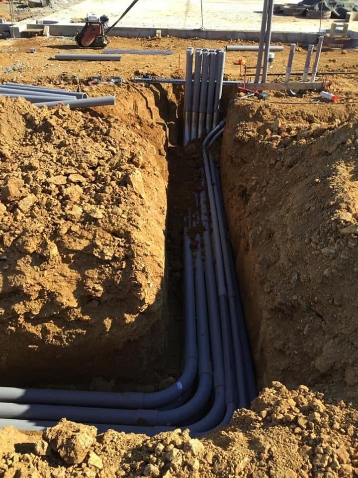 A bank of electrical conduit sweeping up out of an open trench